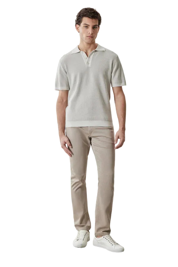 Man wearing a light gray polo shirt and beige pants against a plain background