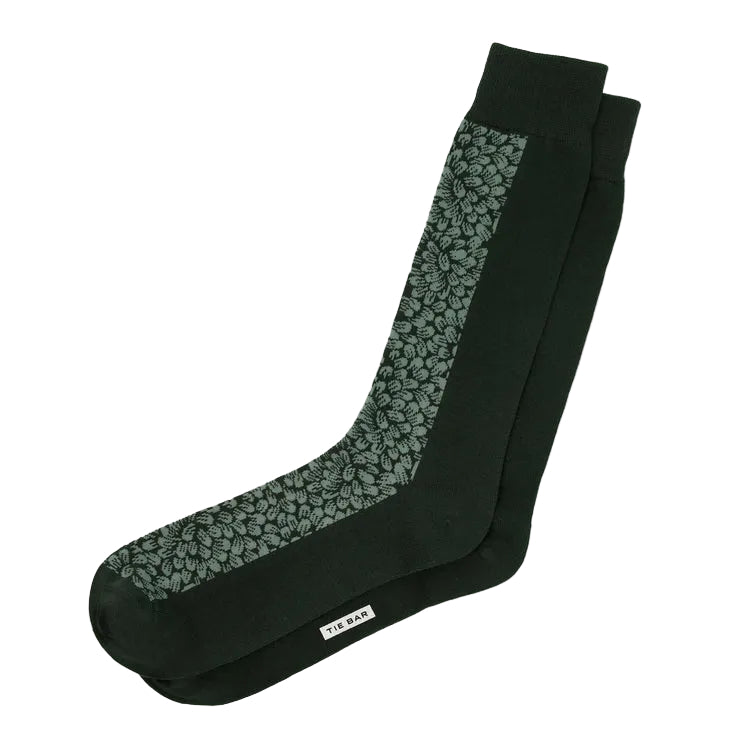 A pair of dark green crew socks with a lighter green leaf pattern on the sides and a small white brand tag reading 'TWEET' near the toe, shown on a light gray background.
