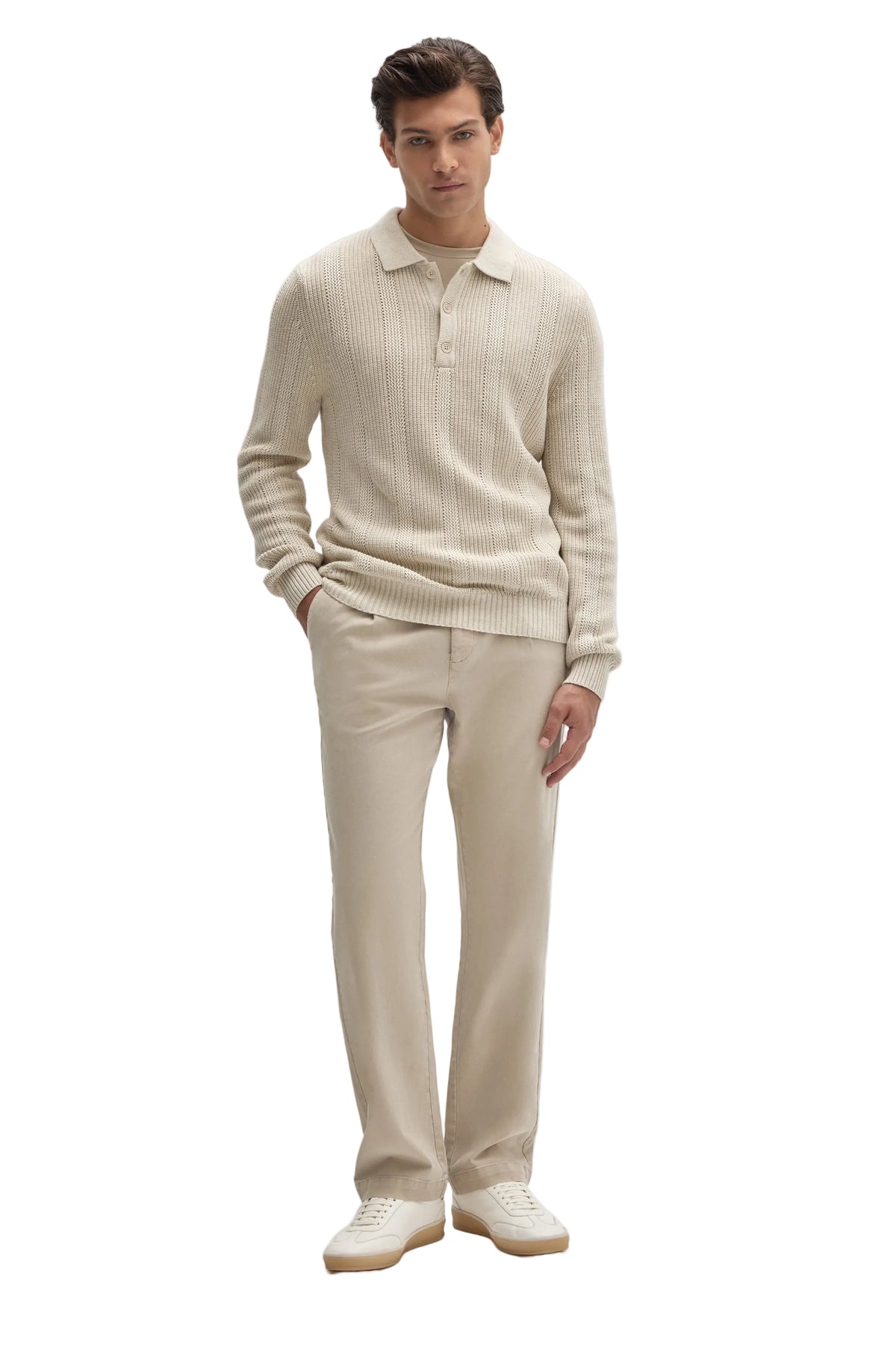 A man modeling a light beige ribbed knit polo sweater and matching trousers with white sneakers, set against a solid light gray background.