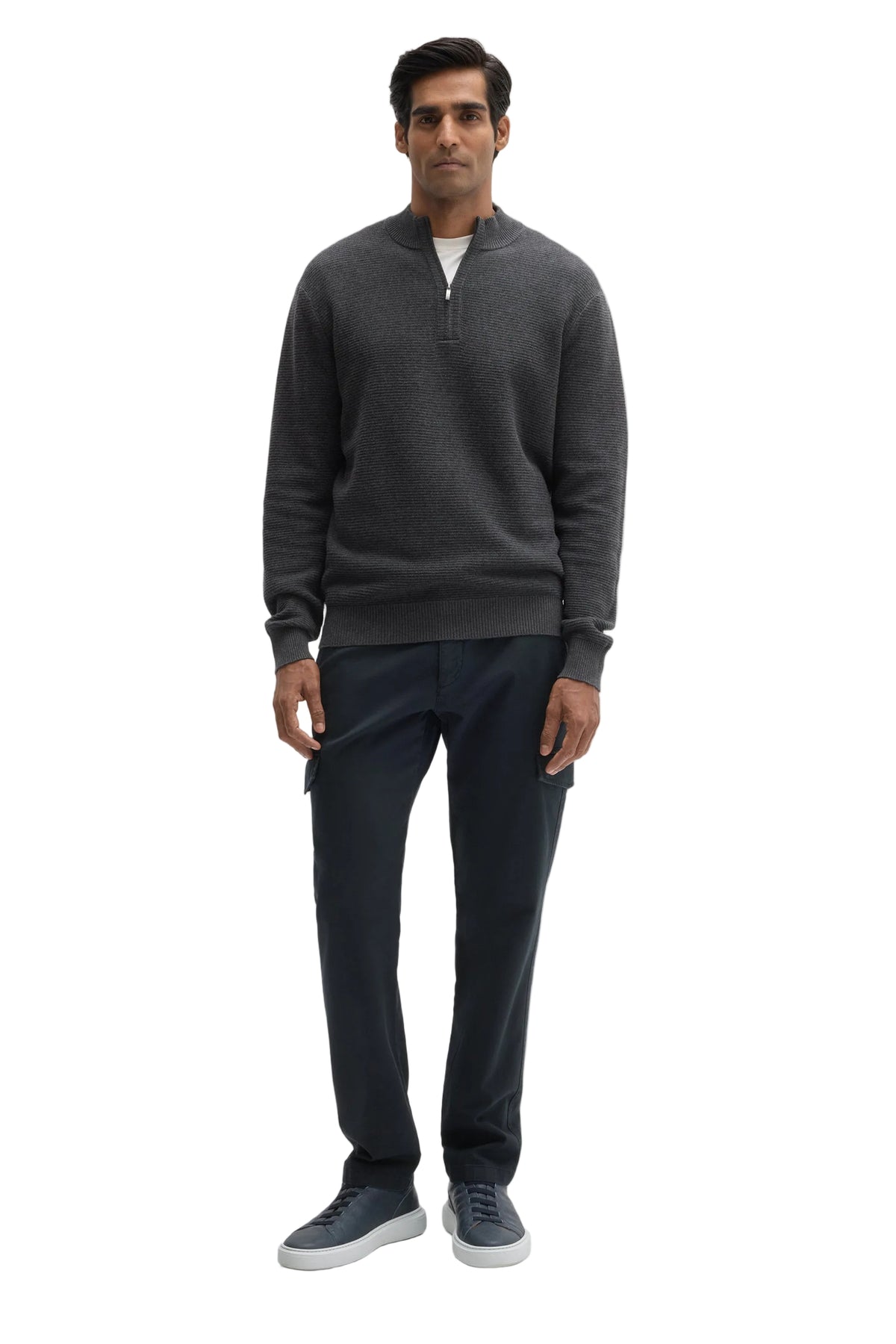 A man modeling a dark gray quarter-zip pullover sweater, dark navy pants, and gray sneakers against a light gray studio background.