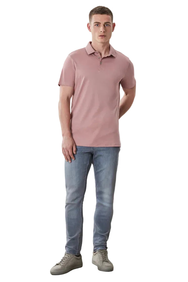 Man wearing a pink polo shirt and blue jeans standing against a plain background