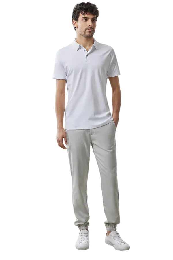 Man wearing a light gray polo shirt and pants with white sneakers against a plain background